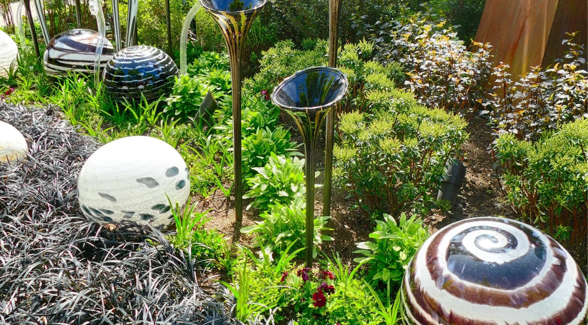 Spotted and spiralled glass spheres and trumpet forms set into the garden beds