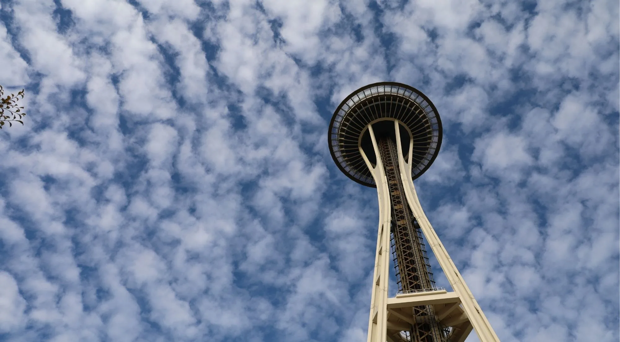 The Space Needle's saucer and elevator shafts photographed from directly below on a cloud-flecked day