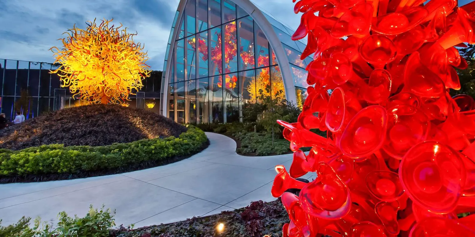 Red glass reeds in the foreground of the Chihuly garden path, the Glasshouse lit behind