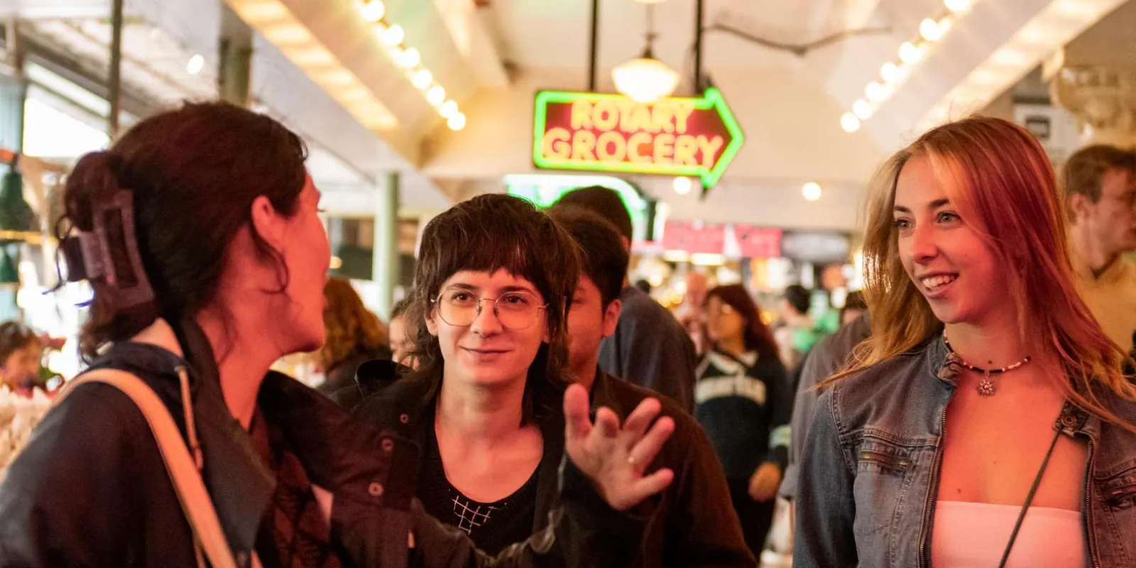 Tour guests laughing under the market's hanging lights beside the Rotary Grocery sign
