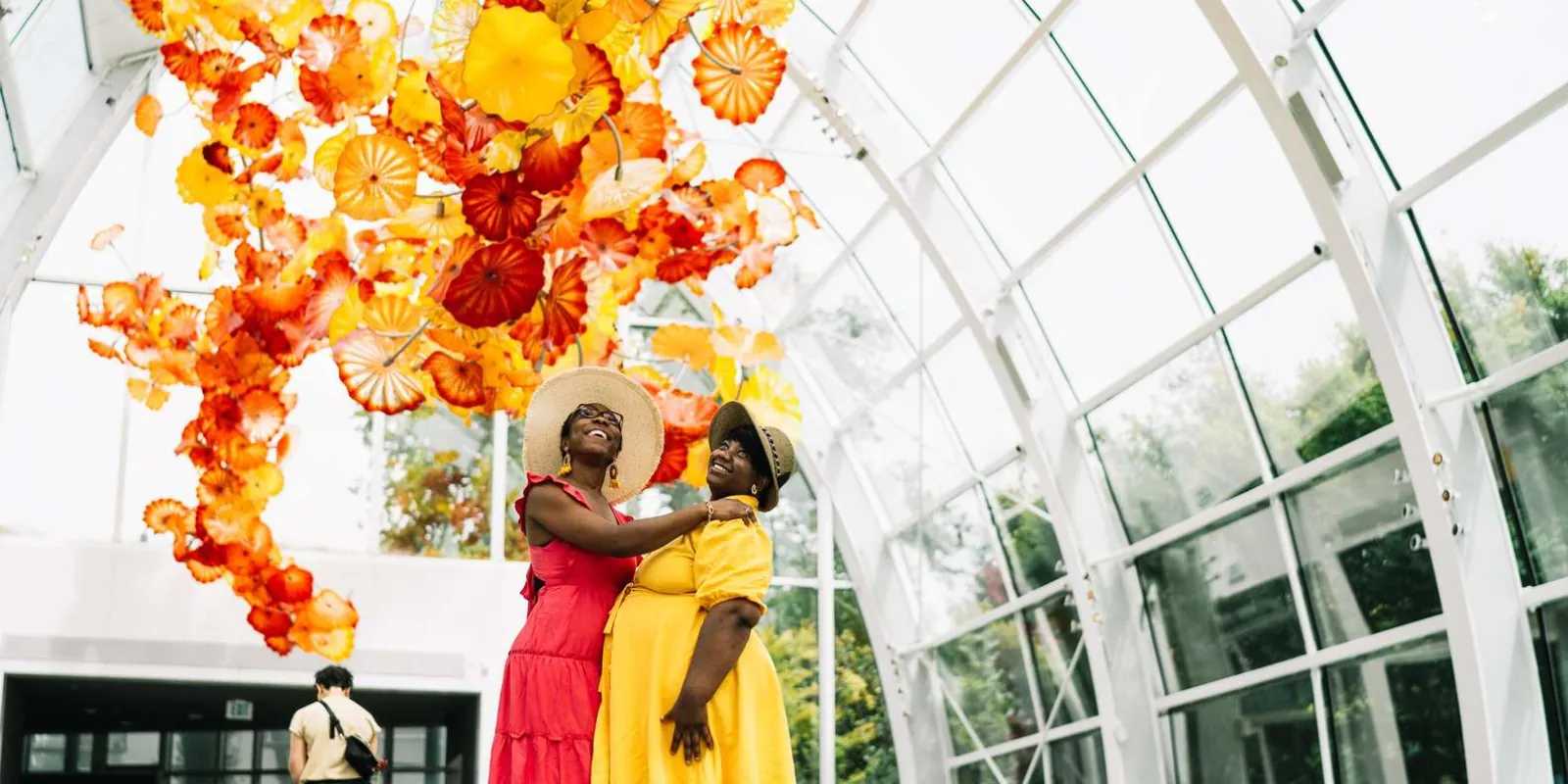 Two visitors standing beneath the 100-foot suspended Glasshouse sculpture in daylight