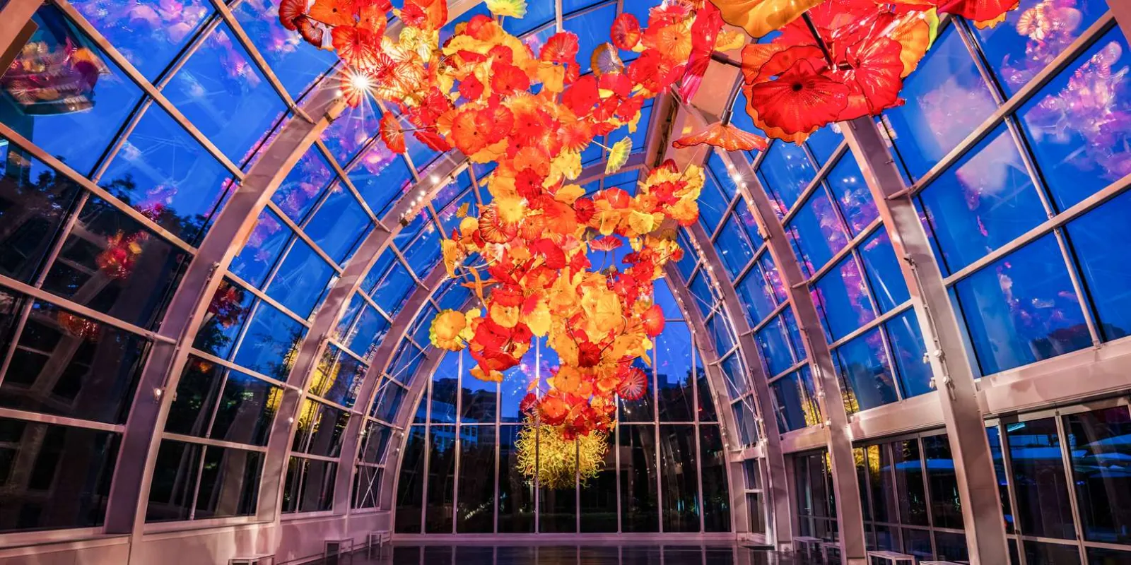 Interior of the Glasshouse at blue hour, the red and orange ceiling sculpture against the darkening sky